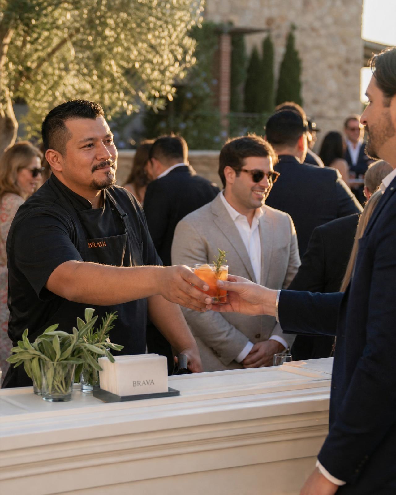 BRAVA server handing a crafted cocktail to a guest at golden hour